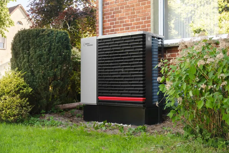 Luft-Wasser-Wärmepumpe im Garten vor einem Einfamilienhaus mit Klinkerfassade