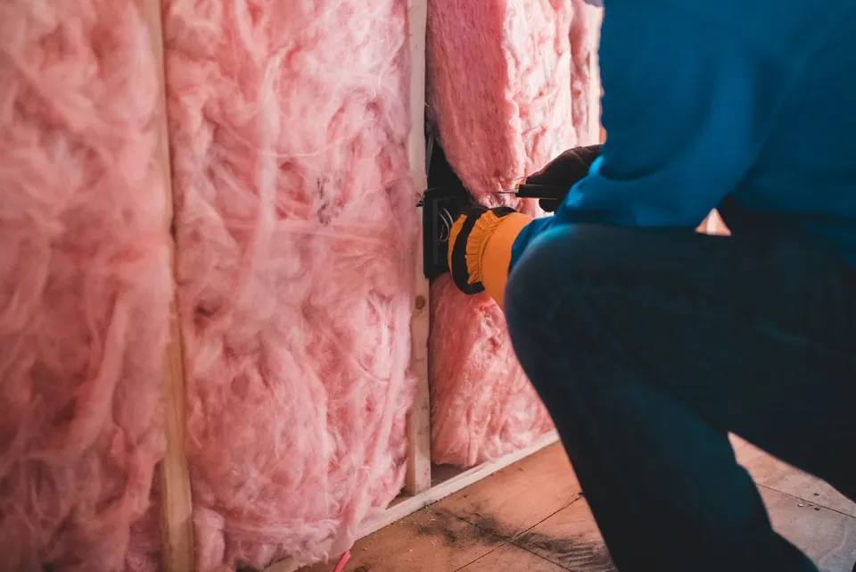Handwerker dämmt eine Wand mit rosafarbener Mineralwolle zwischen den Holzständern