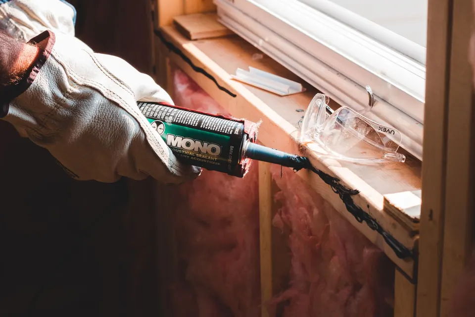 Handwerker dichtet im Fensterrahmen die Fuge neben rosafarbener Wanddämmung ab