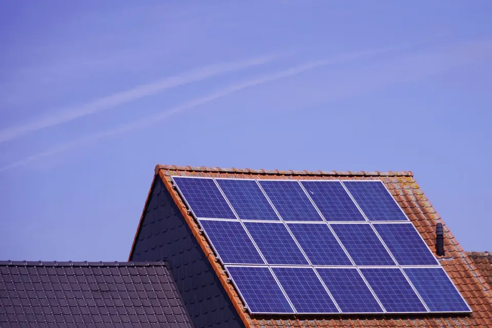 Photovoltaikmodule auf der Dachfläche eines Satteldachs mit roten Ziegeln unter blauem Himmel