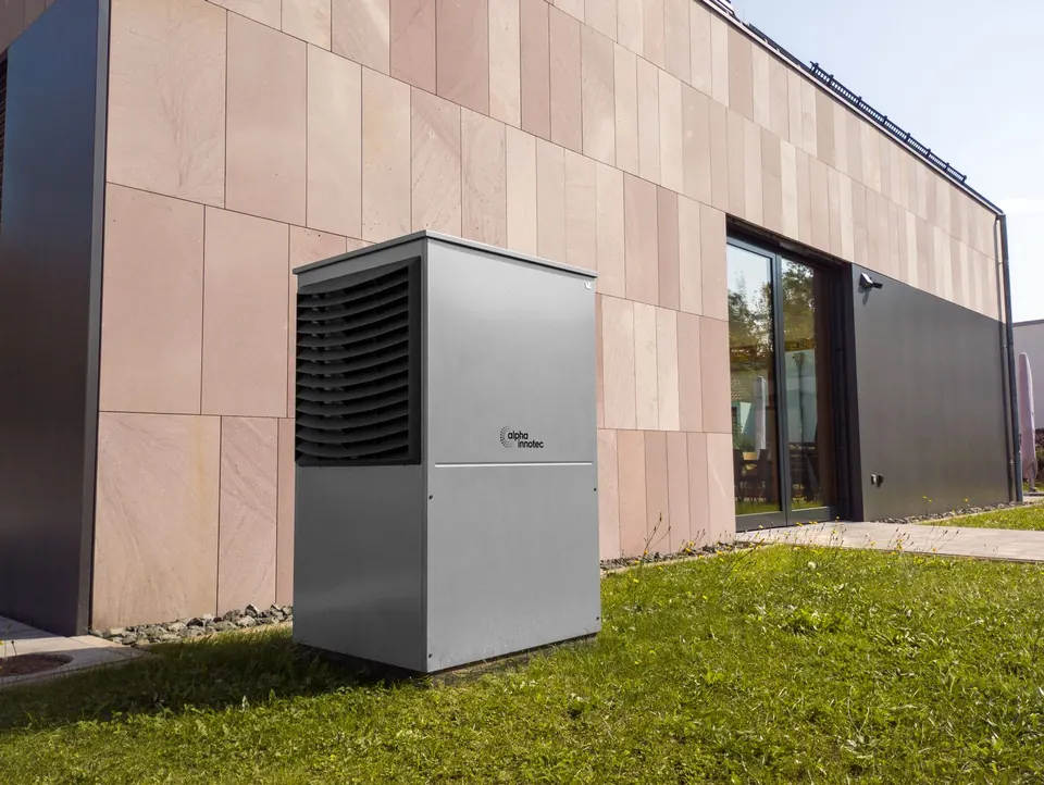 Moderne Wärmepumpe im Garten vor der Fassade eines neuen Hauses